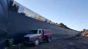 Red water truck parked in front of a long, high wall with reflective panels in Southgate, CA, under a clear blue sky.